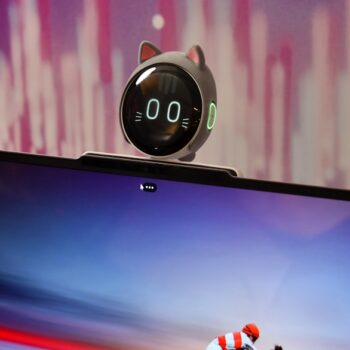 Small round robot with cat ears sits atop a ThinkBook laptop against a purple backdrop.