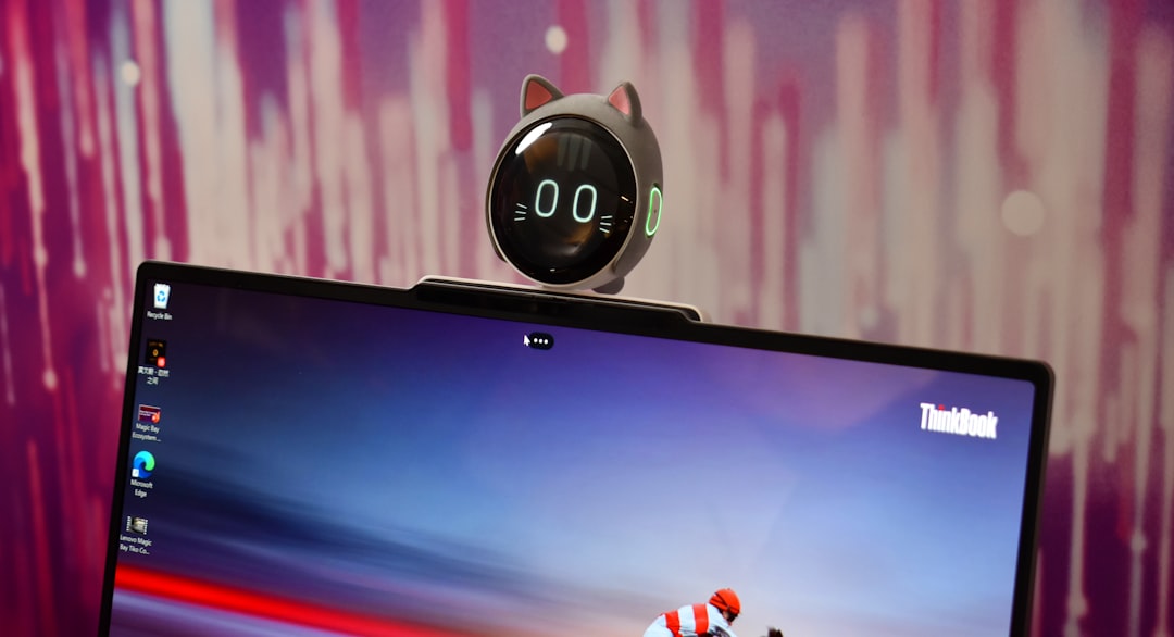 Small round robot with cat ears sits atop a ThinkBook laptop against a purple backdrop.