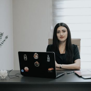 Woman sitting at desk with laptop and plant.