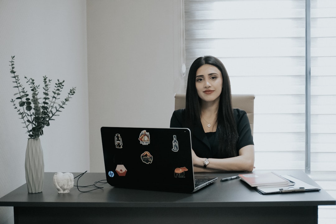Woman sitting at desk with laptop and plant.