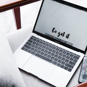 Laptop on a sofa shows the phrase 'Go get it' on screen, with a smartphone nearby on the armrest.