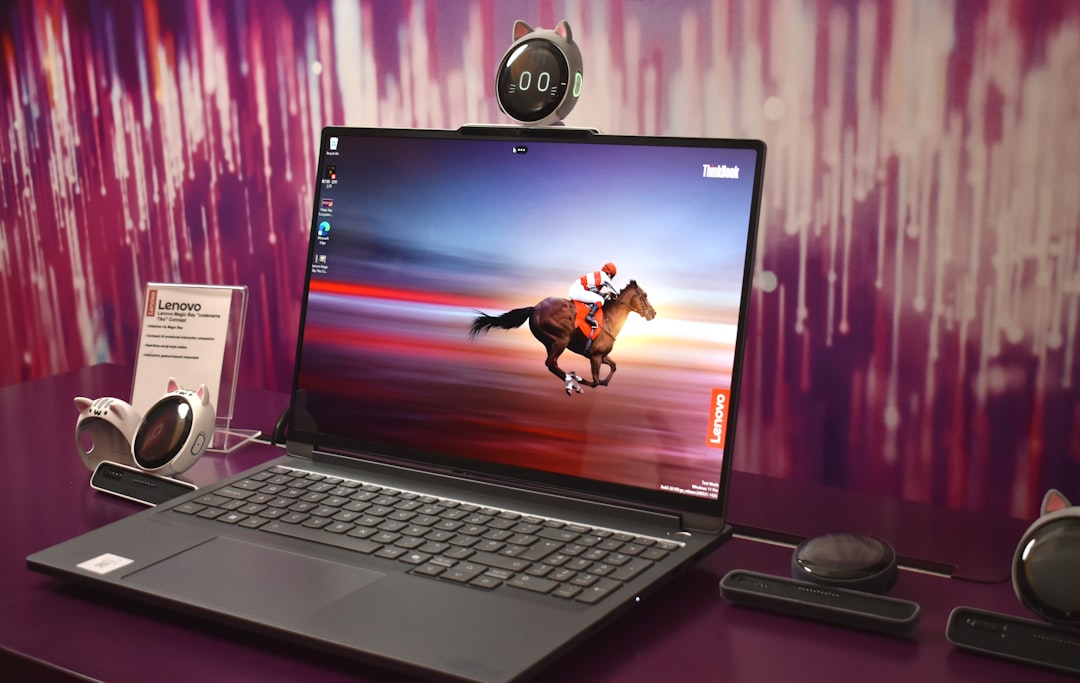 Lenovo ThinkBook laptop on a purple desk displaying a horse rider wallpaper, with a cat-ear webcam perched on top and accessories nearby.