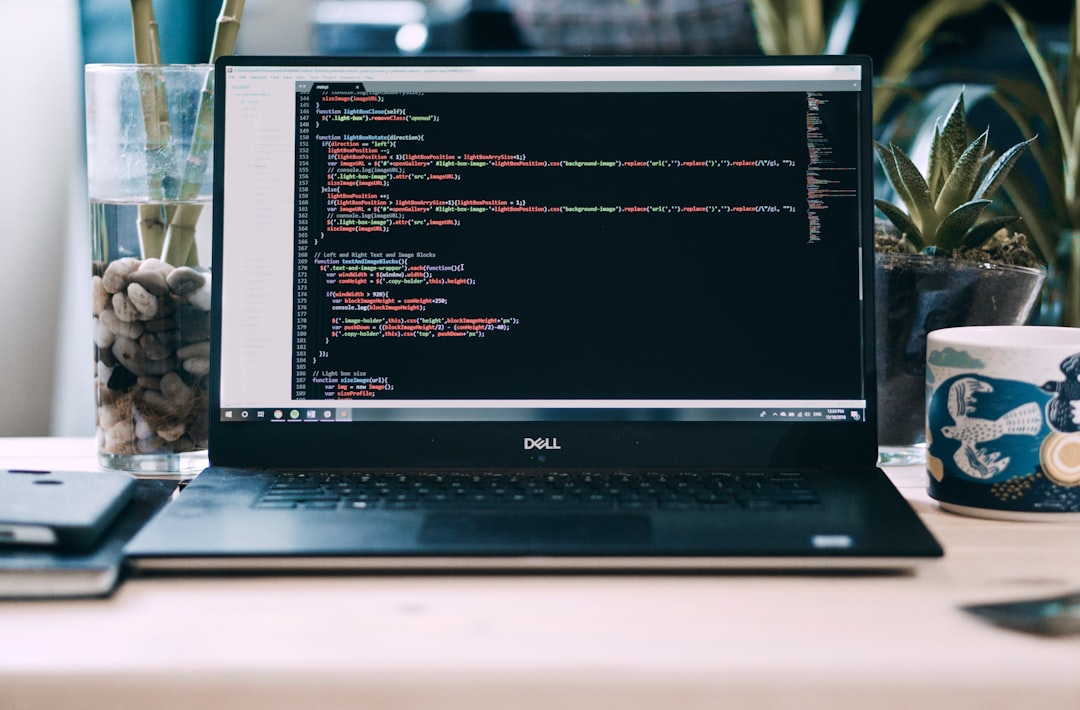 Open Dell laptop on a desk displaying colorful code in a dark editor, with plants and a patterned mug in the background, creating a workspace scene.