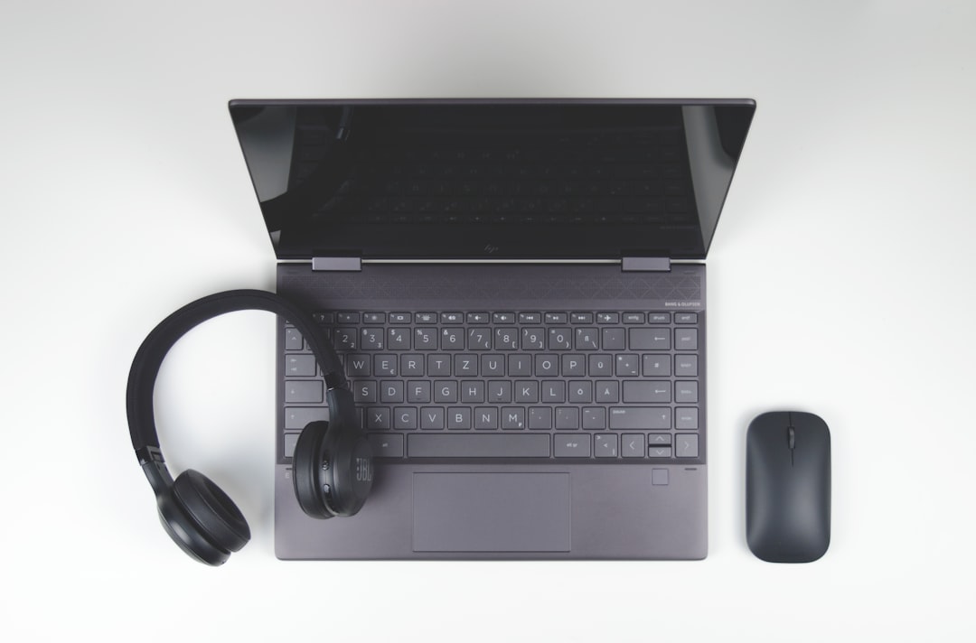 Top-down view of a gray laptop on a white desk, with black over-ear headphones resting on the keyboard and a wireless mouse to the right.