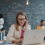 Woman on phone working on laptop in modern office