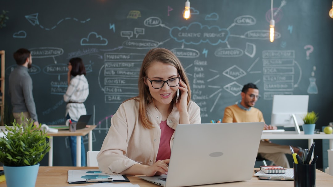 Woman on phone working on laptop in modern office