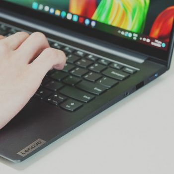 Close-up of hands typing on a Lenovo laptop keyboard with the screen visible in the background.