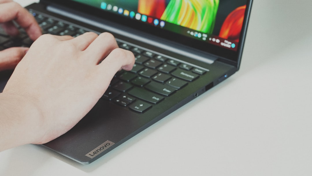 Close-up of hands typing on a Lenovo laptop keyboard with the screen visible in the background.